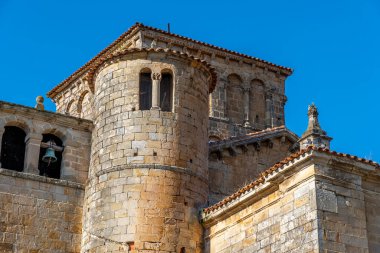 Close-up view of the architectural detail of the Collegiate Church of Santa Juliana in Santillana del Mar, Cantabria, Spain. The medieval stone structures are highlighted against a bright blue sky.