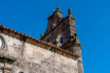 Santillana del Mar, Cantabria, İspanya 'daki tarihi çan kulesinin yakın görüntüsü. Antik taş mimarisi açık mavi gökyüzüne karşı duruyor..
