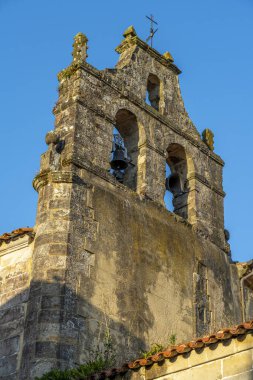 Santillana del Mar, Cantabria, İspanya 'daki tarihi çan kulesinin yakın görüntüsü. Antik taş mimarisi açık mavi gökyüzüne karşı duruyor..