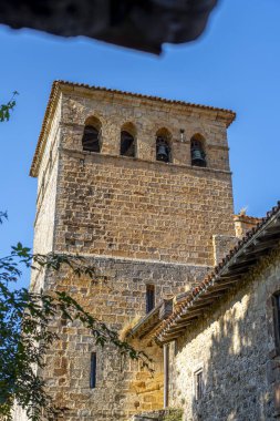 Santillana del Mar, Cantabria, İspanya 'daki Santa Juliana Kolej Kilisesi' nin çan kulesine yakın çekim. Ortaçağ taş mimarisi açık mavi gökyüzüne karşı duruyor..
