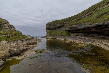 İspanya, Cantabria 'da yemyeşil yosunlarla kaplı katmanlı kaya oluşumlarının üzerinden akan resim gibi bir şelale. Doğa, seyahat ve manzara temaları için ideal.