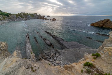 İspanya, Cantabria 'da dramatik gökyüzü, kayalık kıyı şeridi ve kıyı evleri içeren Playa de la Arna üzerinde güzel bir günbatımı. Deniz manzarası, seyahat ve doğa temaları için mükemmel.. 