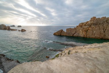 İspanya, Cantabria 'da dramatik gökyüzü, kayalık kıyı şeridi ve kıyı evleri içeren Playa de la Arna üzerinde güzel bir günbatımı. Deniz manzarası, seyahat ve doğa temaları için mükemmel.. 