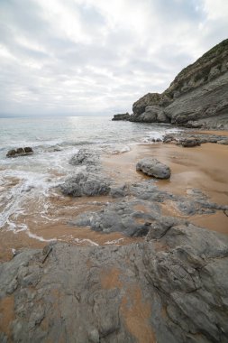 İspanya, Cantabria 'daki Tagle Sahili' nin sakin sahnesinde engebeli kayalar, hafif dalgalar ve geniş bir ufuk görülüyor. Seyahat, doğa ve kıyı temaları için mükemmel..