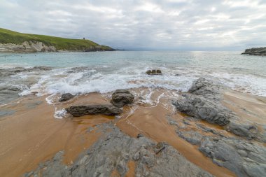 Tranquil scene of Tagle Beach in Cantabria, Spain, showcasing rugged rocks, gentle waves, and an expansive horizon. Perfect for travel, nature, and coastal themes. clipart