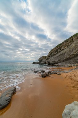 İspanya, Cantabria 'daki Tagle Sahili' nin sakin sahnesinde engebeli kayalar, hafif dalgalar ve geniş bir ufuk görülüyor. Seyahat, doğa ve kıyı temaları için mükemmel..