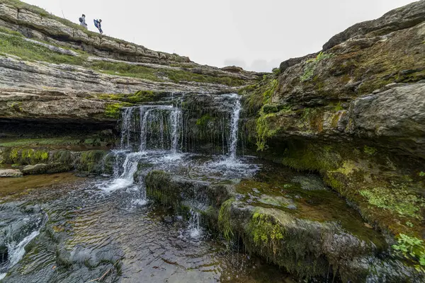 stock image Picturesque waterfall flowing over layered rock formations with lush green moss in Cantabria, Spain. Ideal for nature, travel, and landscape themes.