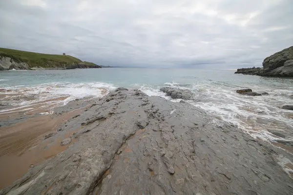 Stock image Tranquil scene of Tagle Beach in Cantabria, Spain, showcasing rugged rocks, gentle waves, and an expansive horizon. Perfect for travel, nature, and coastal themes.