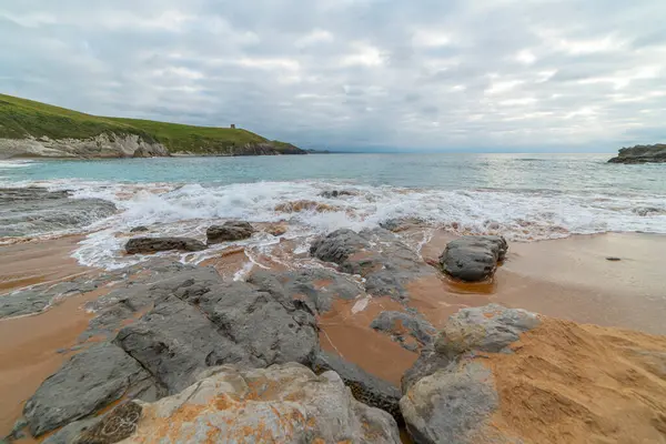 stock image Tranquil scene of Tagle Beach in Cantabria, Spain, showcasing rugged rocks, gentle waves, and an expansive horizon. Perfect for travel, nature, and coastal themes.