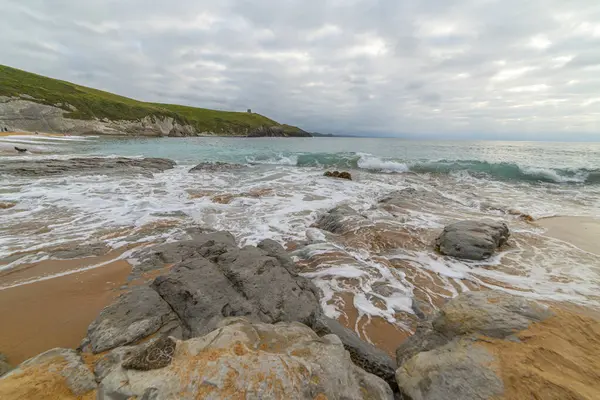 stock image Tranquil scene of Tagle Beach in Cantabria, Spain, showcasing rugged rocks, gentle waves, and an expansive horizon. Perfect for travel, nature, and coastal themes.