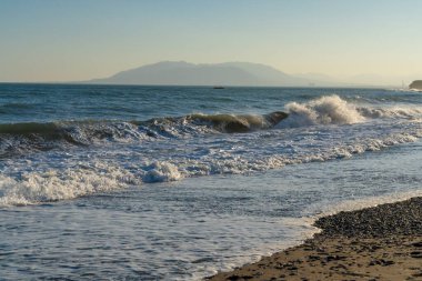 İspanya 'nın Malaga kıyıları boyunca güçlü dalgalar kopuyor ve ufukta uzak dağlar görünüyor. Kıyı enerjisi, doğa ve manzaralı deniz manzarası temaları için ideal