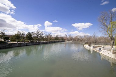 İspanya 'nın Aranjuez şehrinde bereketli ağaçlar ve tarihi binalarla çevrili sakin bir nehir akmaktadır. İnsanlar gün ışığında huzurlu atmosferin tadını çıkararak kıyıda yürür..