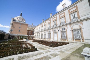 Ziyaretçiler, Aranjuez Kraliyet Sarayı 'nı keşfediyor. Etrafı titizlikle çevrilmiş bahçelerle çevrili, açık mavi bir gökyüzü altında..