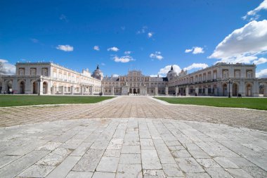Ziyaretçiler, İspanya 'nın Aranjuez kentinin büyük mimarisine ve geniş bahçelerine hayranlık duyuyor. Güneş ışığı, canlı mavi gökyüzüne karşı tarihi yapıları aydınlatıyor..
