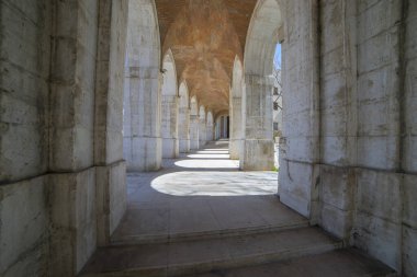 Ziyaretçiler, 18. yüzyıldan kalma anıtsal bir kraliyet konutu olan Palacio de Aranjuez 'deki eski kemerlerin çarpıcı geçitlerinde geziniyorlar..