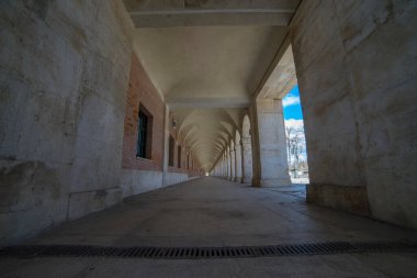 Ziyaretçiler İspanya 'nın Aranjuez kentindeki büyüleyici Eski Yay geçidinde geziyorlar ve şu anda müze olarak hizmet veren kraliyet sarayının yanındaki zarif 18. yüzyıl mimarisini sergiliyorlar..