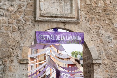 Ziyaretçiler Brihuega 'daki De la Lavanda Festivali' ni kutlamaya hazırlanırken kemer yolunu renkli afişler ve kurdeleler süslüyor. Bu etkinlik lavanta ve yerel kültürü vurguluyor.