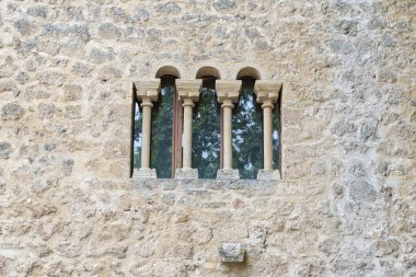 Brihuega, Guadalajara 'da, kırsal bir duvarın desenli yüzeyine karşı dört kolona sahip tarihi taş pencere. Yapı, bölgenin zengin mimari mirasını yansıtıyor..