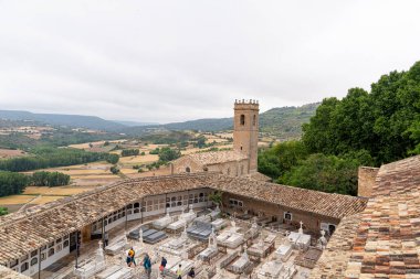 Ziyaretçiler, sakin bir öğleden sonra bulutlu bir gökyüzü altında, Castilla-La Mancha 'nın tipik bereketli tepeleri ve tarlalarıyla çevrili Brihuega' daki antik mezarlığı keşfediyorlar..