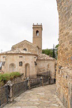 Brihuega 'da, geleneksel İspanyol mimarisi ile süslenmiş iyi korunmuş tarihi binalar ve bulutlu gökyüzünün altında görünen bir çan kulesi bulunan bir kaldırım taşı yolu esiyor..