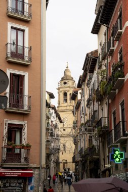 Ziyaretçiler bulutlu bir günde Pamplona 'nın dar sokaklarında dolaşarak büyüleyici mimari ve canlı mağazalarla çevrili tarihi bir saat kulesine yaklaşıyorlar..