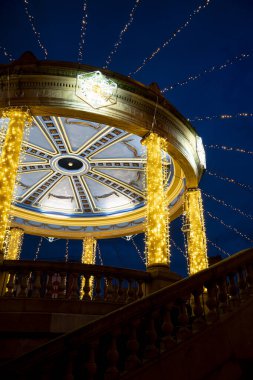 Plaza del Castillo 'da parlak ışıklı çardak duruyor. Karmaşık tasarımlar ve altın ışıklar sergiliyor. Akşam gökyüzü sihirli bir dokunuş ekliyor, Pamplona 'daki şenlikli atmosferi güçlendiriyor..