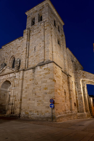 In Zamora, Castilla y Leon, a grand stone structure stands illuminated at night. The intricate details of the architecture are highlighted, showcasing the history embedded in the walls.