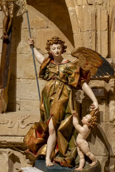 Zarif bir melek heykeli zarif bir şekilde duruyor, bir asa tutuyor ve tarihi Colegiata de Santa Maria la Mayor de Toro 'da küçük bir çocuğa rehberlik ediyor. Karmaşık işçiliği sanatın altını çiziyor..