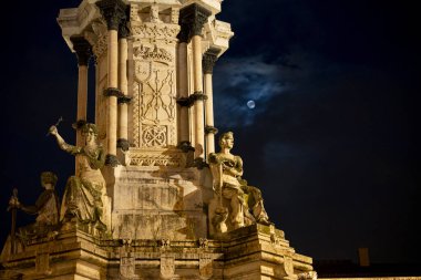 Monumento a los Fueros, Pamplona, Navarra 'da ay ışığıyla aydınlatılmış gökyüzünün arka planına karşı karmaşık heykeller sergiliyor. Yapı aydınlatılmış, sanatsal ayrıntılarını vurguluyor..