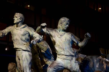 Pamplona 'daki bronz heykel, geleneksel katılımcıları tasvir eden dinamik figürlerle San Fermin' in ruhunu yansıtıyor. Sanat eserlerinde şenlikler sırasında güç ve heyecan gösteriliyor..