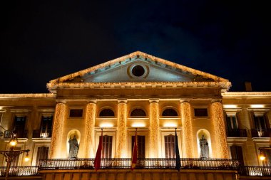 Güzel Pamplona belediye binası Navarra geceleri aydınlanıyor ve büyük mimarisi ve heykelleri sergileniyor. Akşam rüzgarında dalgalanan bayraklar, canlı bir atmosfer yaratıyor..