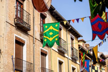 Geleneksel Ortaçağ Fuarı sırasında kültür ve mirası kutlamak için Alcala de Henares 'in tarihi sokaklarını süsleyen şenlikli afişler, canlı ve renkli bir ortam yaratıyor..