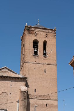 Zamora 'daki tarihi bir kilisenin uzun tuğla kulesinde ikiz çanlar sergileniyor. Yapı parlak mavi bir gökyüzüne karşı duruyor, mimari özelliklerini vurguluyor..