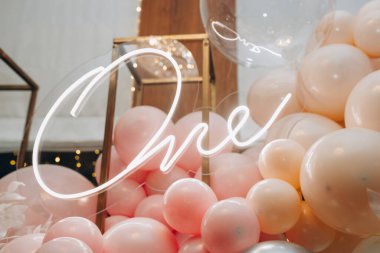 birthday celebration concept, neon lettering one year, pink, white and beige inflatable balloons. High quality photo