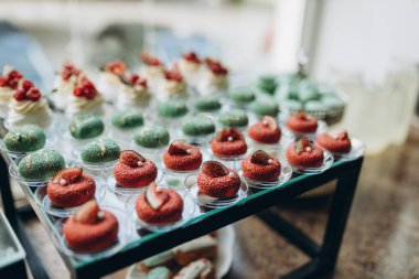 Candy bar. White wedding cake decorated by flowers standing of festive table with deserts, strawberry tartlet and cupcakes. Wedding. Reception Tartlets. High quality photo