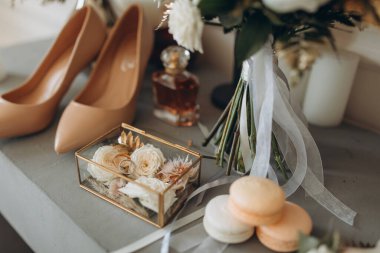 gold wedding rings next to the bride's white shoes, a bouquet of flowers and boutonnieres on a glass table. High quality photo