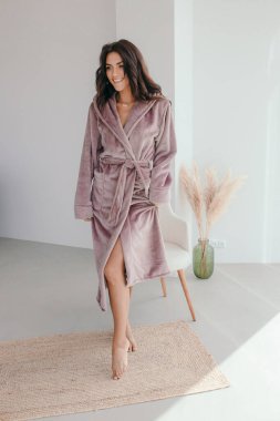 Beyaz bornozlu bir kızın büyük pencereli bir odada küvetin yanında durduğunu hayal et. Yüksek kalite fotoğraf