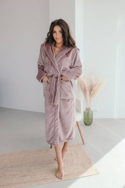 Beyaz bornozlu bir kızın büyük pencereli bir odada küvetin yanında durduğunu hayal et. Yüksek kalite fotoğraf