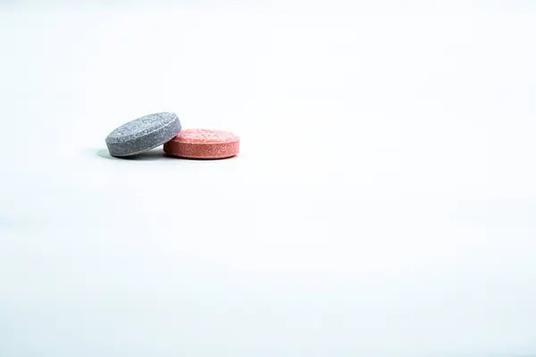 İki renkli Antacid, biri diğerine yaslanıyor, beyaz bir arka planı var..
