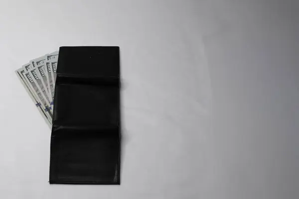 Beyaz arka planda yüz dolarlık banknotlar olan siyah bir cüzdan..