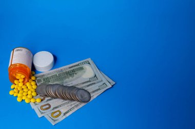 A pill bottle with yellow pills spilled out on hundred dollar bills and silver dollars. The concept is the expense of drugs that are taken like candy and abused. Top view. clipart