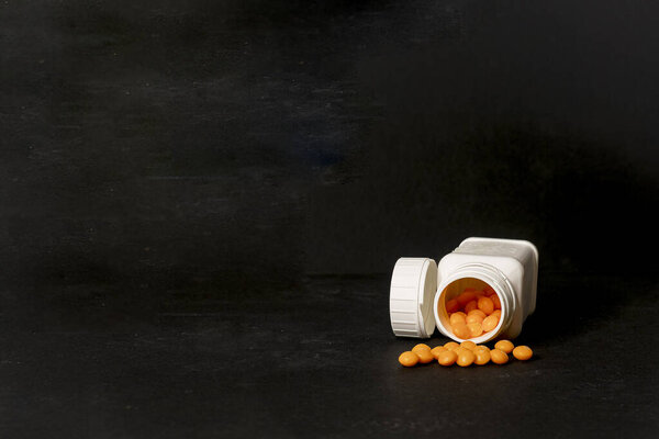 Белая бутылка с таблетками с апельсинами. Чёрный фон. Концепция показала, что к наркотикам относятся как к конфетам.