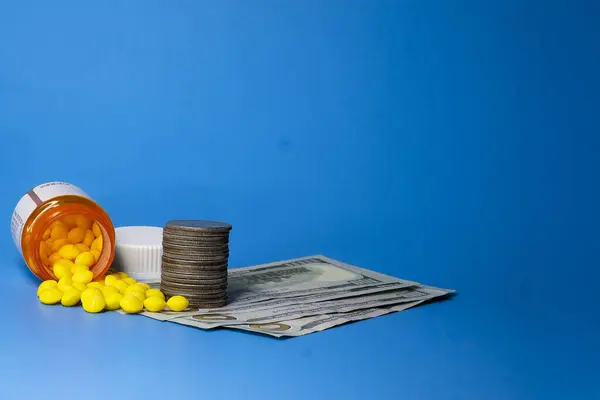Hunderd dolar ve gümüş dolarların üzerine sarı haplar dökülmüş bir hap şişesi. Konsept, şeker gibi alınan ve suistimal edilen uyuşturucuların gideri. Ön görünüm.