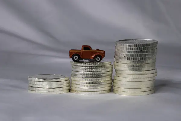 Bozuk para yığınının üzerinde oyuncak bir kamyon. Araçların düşük giderlerinin artmaya devam ettiğini gösteren kavram. Satın alma fiyatı ve devam eden bakım zammı.