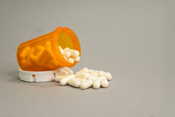 Оранжевый рецептурный контейнер на боку с капсулами, пролитыми перед ним. Серый фон