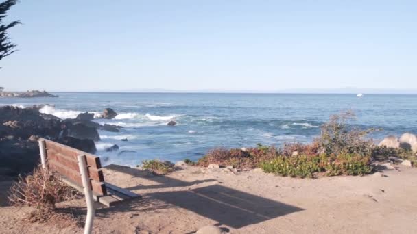 海岸沿いのオーシャンビーチ 空の木製ベンチ 海の波がクラッシュし モントレーベイ 17マイルドライブ カリフォルニア州海岸 パシフィックグローブビーチフロントウォーターフロント遊歩道 水辺公園 シーサイドビュー — ストック動画