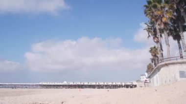 Palmiye ağacı ve ahşap kristal iskele, California Okyanus Sahili, ABD. San Diego kıyısındaki Mission sahilindeki yazlık evlerde. Beyaz evler, gökyüzü, deniz kıyısındaki bungalovlar