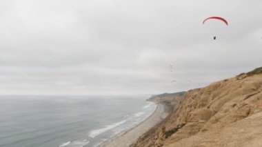 İnsanlar yamaç paraşütü yapıyor, Torrey Pines uçurumu ya da blöf. Paraglider gökyüzünde süzülüyor, paraşütle, uçurtmayla veya kanatla uçuyor. Eğlence amaçlı spor hobisi. Okyanus kıyısı, San Diego, Kaliforniya ABD. Paraşüt uçuşu