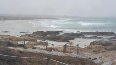 Okyanus kumlu kum tepeleri, Monterey doğası, California sisli kıyıları, ABD. Sisli yağmurlu sonbahar ya da kış havası, gri bulutlu gökyüzü. Tahta merdivenler, kıyıdaki patika yolu soğuk deniz dalgalarının yanında. Sakin atmosfer.