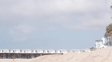 Palmiye ağacı ve ahşap kristal iskele, California Okyanus Sahili, ABD. San Diego kıyısındaki Mission sahilindeki yazlık evlerde. Beyaz evler, gökyüzü, deniz kıyısındaki bungalovlar